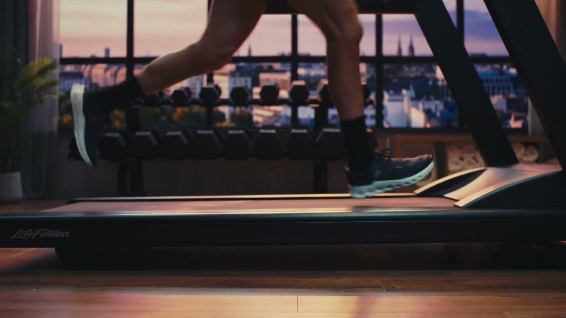 Life Fitness Atmos treadmill side-on with full city skyline through the LED volume window