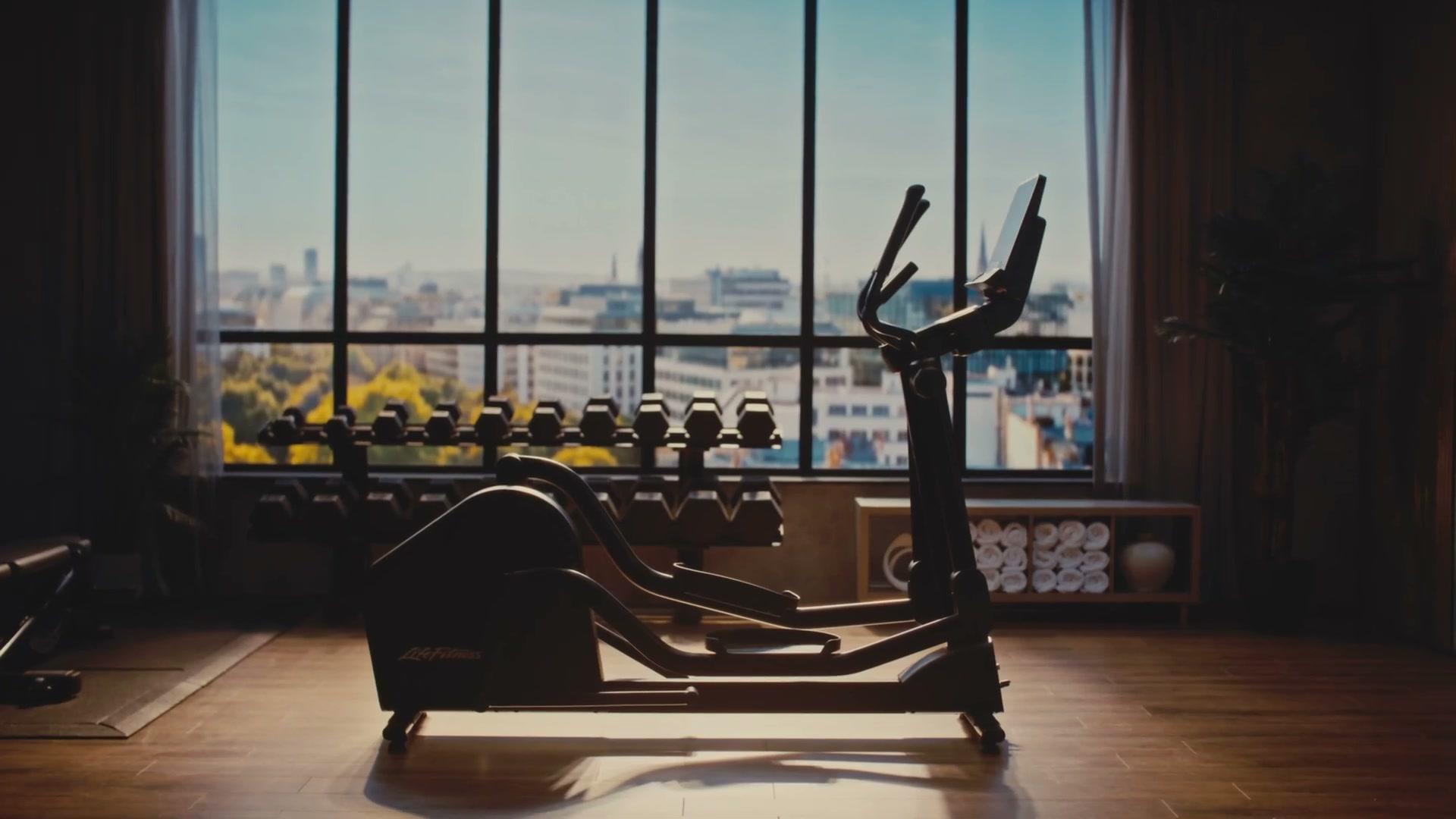 Life Fitness Atmos elliptical, wide hotel-gym scene with daylight skyline through the LED volume window