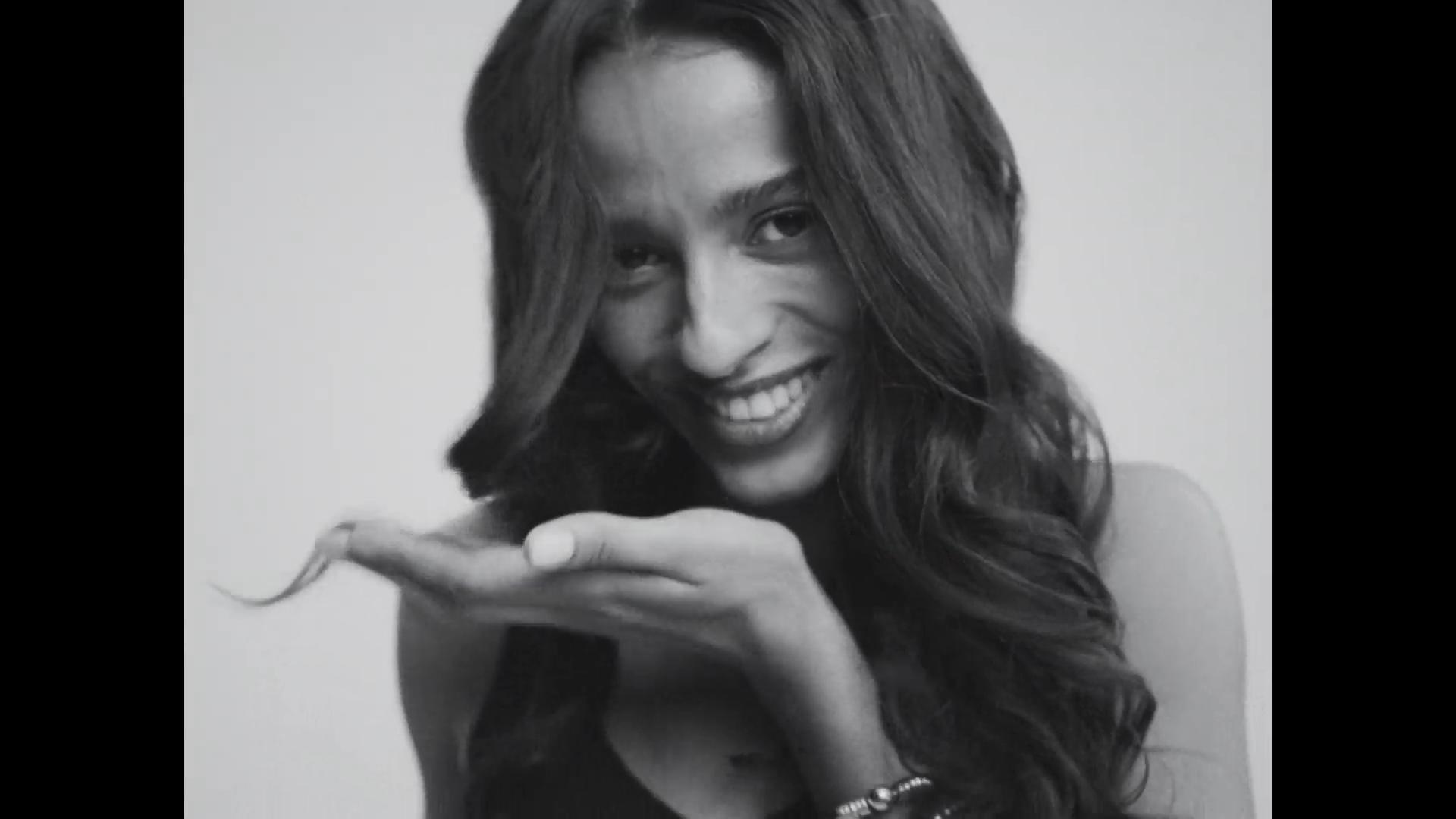 B&W close-up of brunette model laughing while twirling a hair strand on her finger.