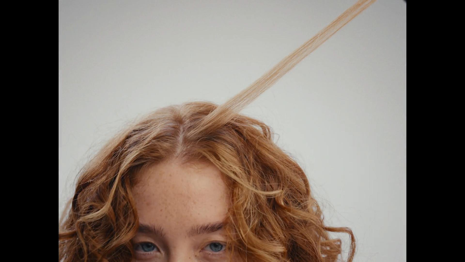 Top half of redhead model with freckles; curly hair with strand flying in motion blur.