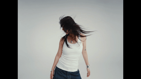 Asian-presenting model in white tank tossing long black hair in motion blur on pale cyc.