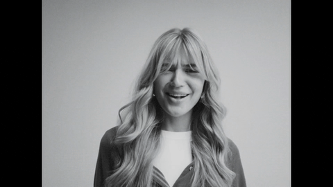 B&W close-up of smiling blonde model, eyes closed, laughing.