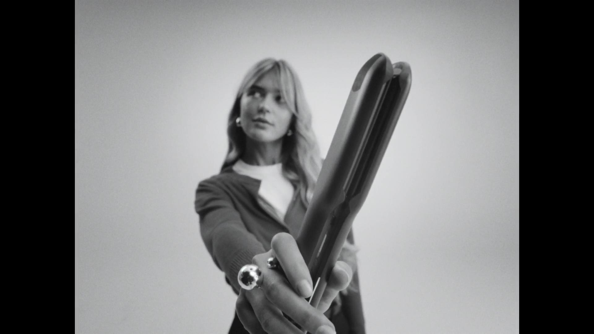 Black-and-white shot of blonde model holding Cloud Nine hair straightener to camera with silver rings on hand.