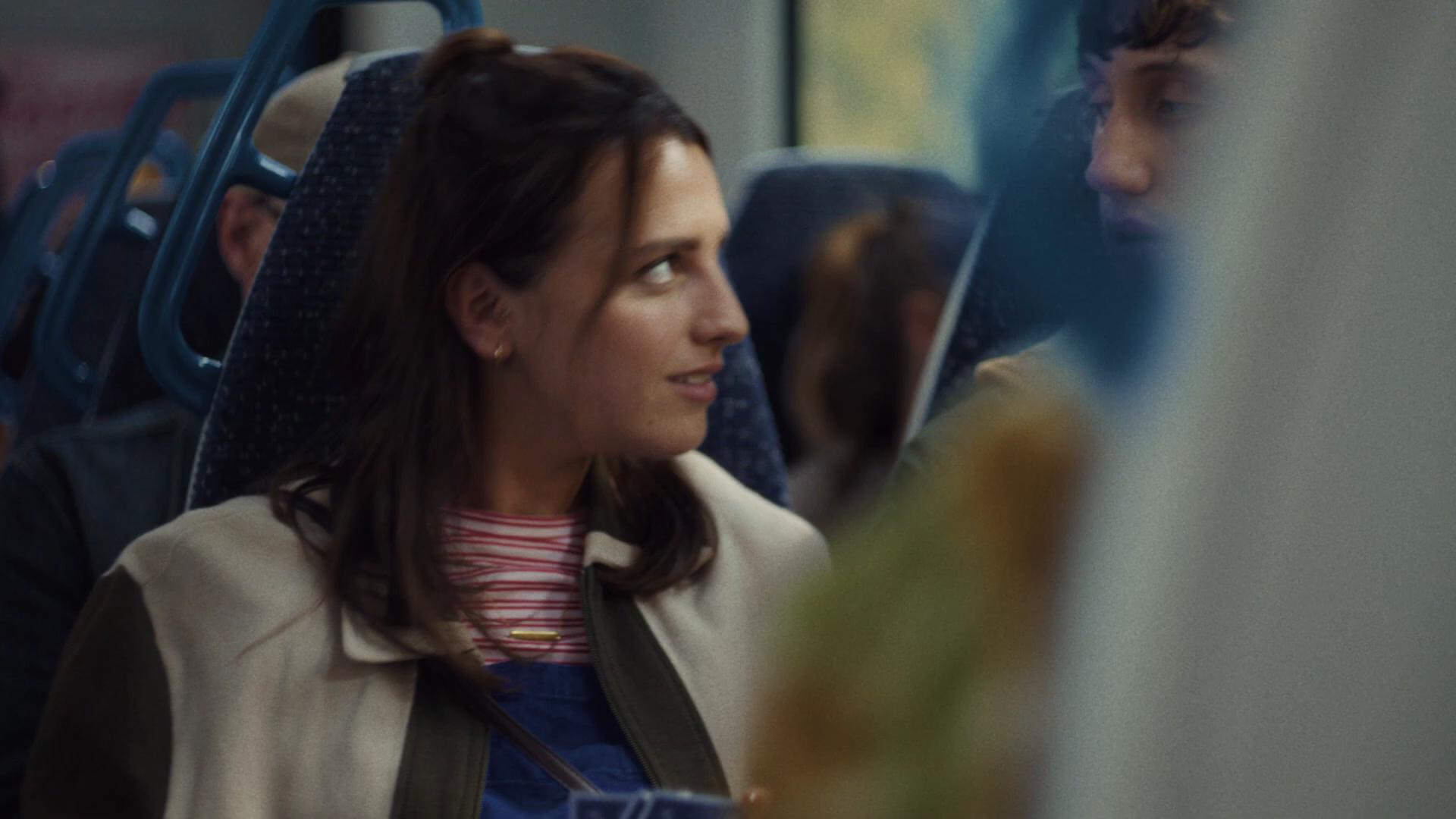 MCU of Lily on the Thameslink train, half-up hairstyle, mock-glum sympathetic frown directed at Callum