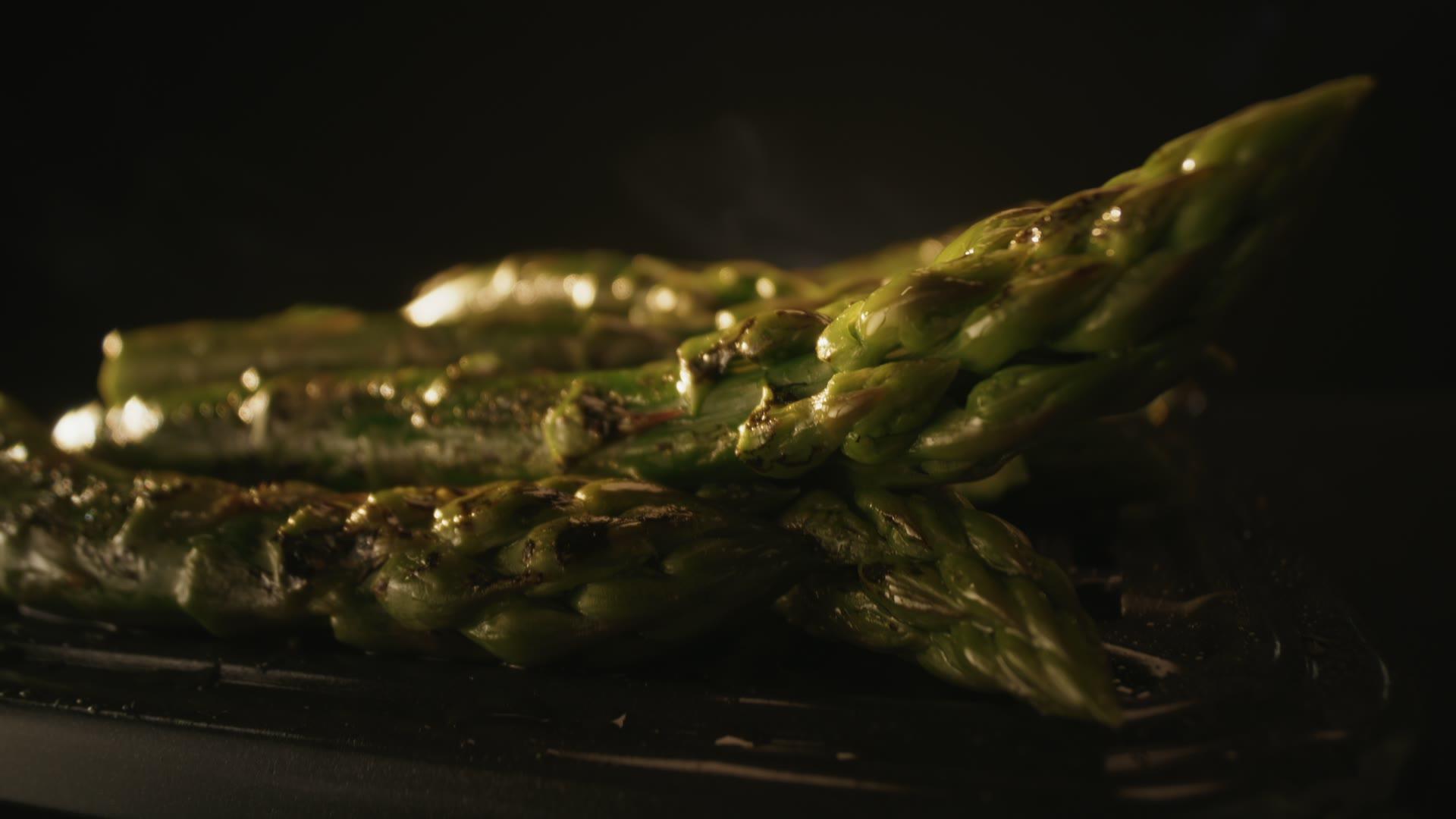 Glistening charred asparagus stacked on a black background, 350fps food beauty.