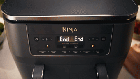 Two hands pulling open both drawers of the Ninja DZ300, revealing stuffed-vegetable bake and golden filo rolls.