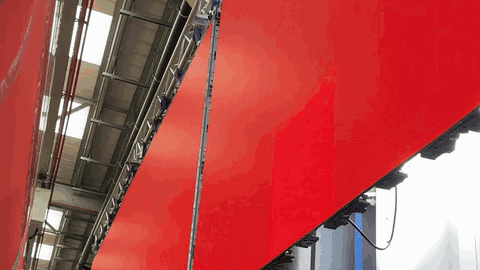 BTS — LED panel volume powered up displaying a solid red test fill, two angled walls catching the light dramatically, NANLITE fixture and crew silhouette in frame