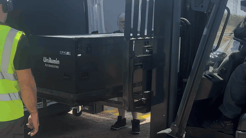 BTS strike — Unilumin LED panel flight case being lifted off a forklift outside the depot during load-out, crew member in hi-vis directing