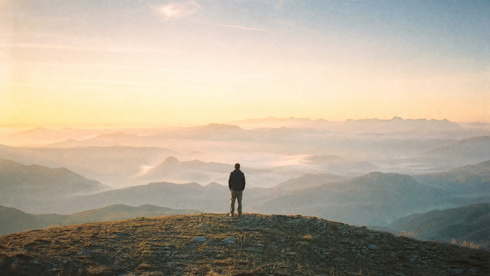 A person on a mountain summit at sunrise looking out over misty peaks